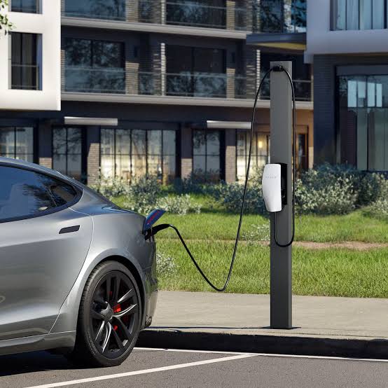 Silver Tesla charging at a pedestal Wall Connector outside an apartment building