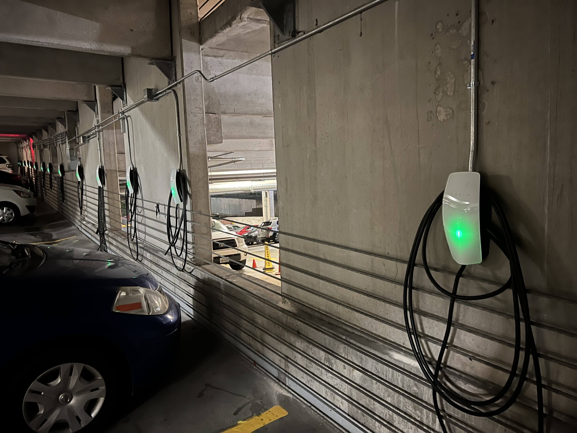 Row of installed Tesla Wall Connectors with green status lights in a parking garage